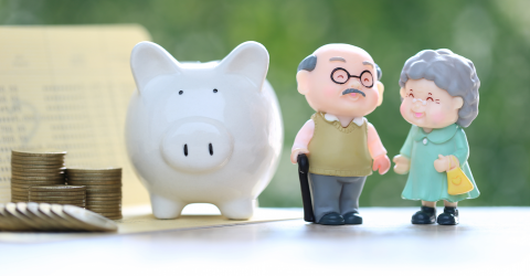 Poppetjes van een senior koppel dat hand in hand staat naast een wit spaarvarken en een stapel muntgeld